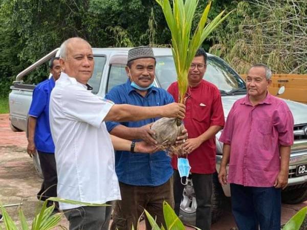 Mohd Soffi (kiri) menyampaikan anak pokok kelapa pada Majlis Penyerahan Anak Benih Bagi Program Penanaman Kelapa Keliling Rumah (KKR) di Balai Raya Kampung Mambang, di sini.