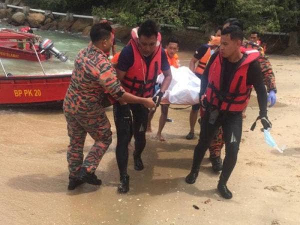 Anggota bomba mengusung mayat mangsa selepas ditemukan terapung di celah batu di Pantai Teluk Batik hari ini. - Foto JBPM Perak.