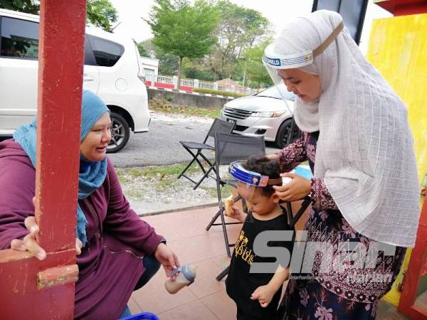 Nur Amira melihat anaknya dipakaikan alat pelindung muka sebelum dibenarkan masuk ke dalam tadika.