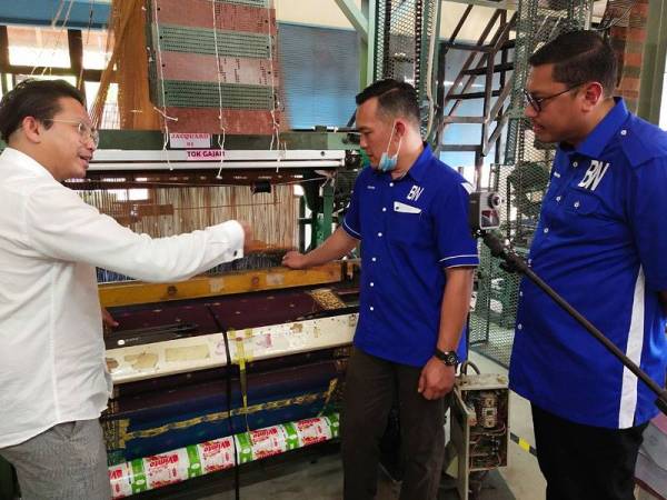 Mohd Sharim (tengah) diberikan taklimat ringkas oleh Affendi (kiri) berhubung operasi pengeluaran Pusat Tenun Pahang Diraja Felda di Chini semalam.