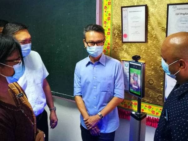 M Packiam (kiri) menjalani pemeriksaan suhu badan menggunakan alat pengimbas haba yang disumbangkan kepada sekolah berkenaan sambil disaksikan Sze Han (dua dari kiri).