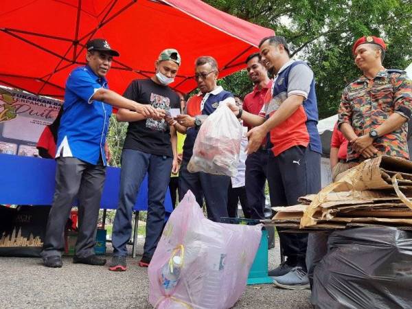 Abd Rahim (kiri) dan Ismail (tengah) menyampaikan hadiah kepada penduduk yang terlibat dalam program Trash To Cash di Bandar Dara, hari ini.