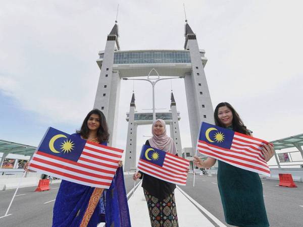 (Dari kanan) Ng Phei Jin, 31, Nursyasya Nadhirah Zabidi, 25, dan B Natasha Dharwahne, 30, memegang Jalur Gemilang sempena sambutan 50 Tahun Rukun Negara berlatar belakangkan Jambatan Angkat Terengganu.