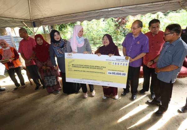 Rina menyampaikan 'mock cheque' kepada Rokiah (empat kanan) ketika melakukan kunjungan ke Kampung Sungai Tembak B hari ini.
