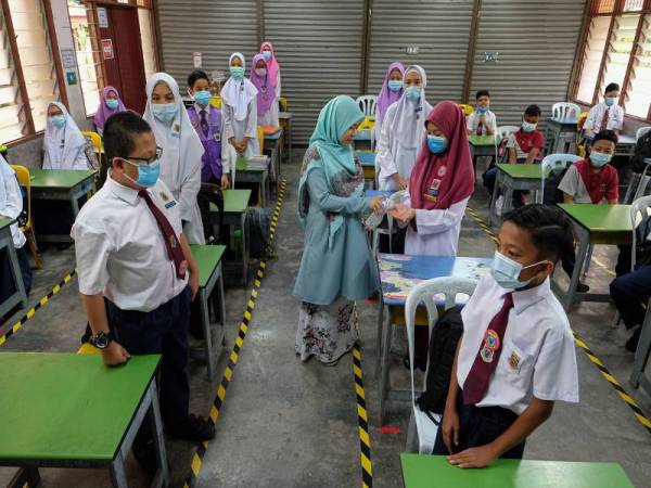 Guru Kelas 6 Topaz, Khairun Hanisah 28, membantu murid-murid menggunakan cecair sanitasi sebelum memulakan sesi pembelajaran.- Foto Bernama