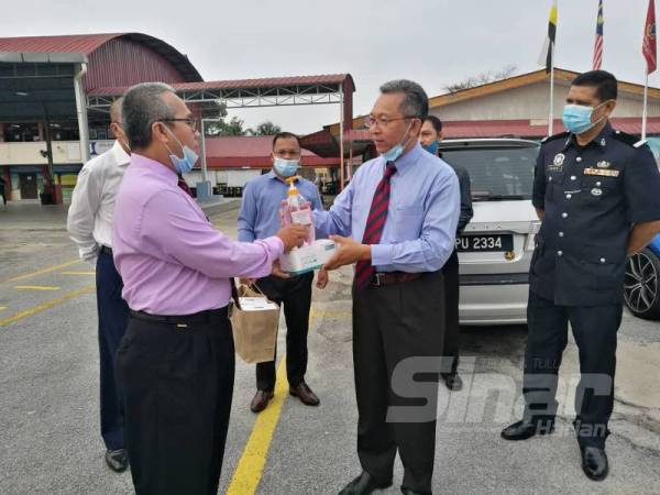 Azizul Kama (kanan) menyerahkan sumbangan pelitup muka dan cecair pensanitasi tangan kepada Noor Azman di perkarangan SK Jelapang hari ini. 