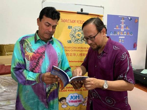 Johari (kanan) menunjukkan sesuatu di dalam buku yang dihadiahkan kepada Mustapha di sini semalam.