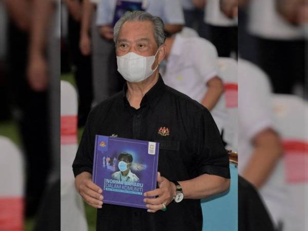 Perdana Menteri, Tan Sri Muhyiddin Yassin memegang buku 'Pembudayaan Norma Baharu Komuniti' terbitan Kementerian Kesihatan yang dilancarkan beliau pada Kempen Pembudayaan Normal Baharu di Kompleks Sukan Pagoh, Muar hari ini. -Foto Bernama