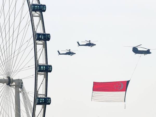 Helikopter Chinook yang membawa bendera kebangsaan diiringi helikopter Apache ketika sambutan Hari Kebangsaan hari ini. - Foto AFP