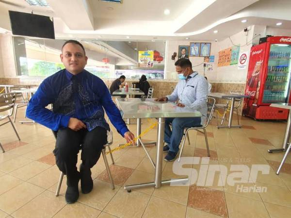 Azeem Qusairy (kiri) menunjukkan pendekatan yang digunakan di Restoran Nasi Kandar Pelita untuk memastikan penjarakan fizikal dalam kalangan pelanggan diamalkan.