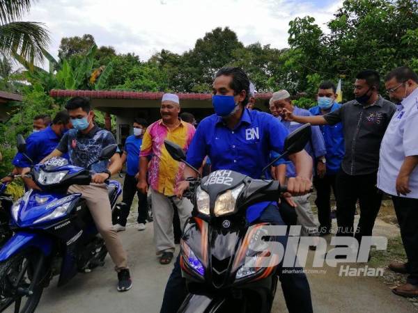 Khairy Jamaluddin menunggang motosikal pada program Ziarah Kasih di Felda Besout 2 di sini hari ini yang turut dihadiri calon BN, Mohd Zaidi Aziz.