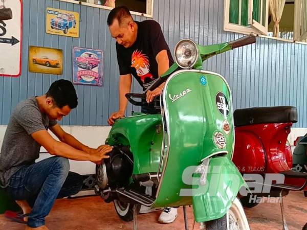Tuan Muhamad Amin (duduk) membaik pulih Vespa sambil diperhatikan ayahnya.