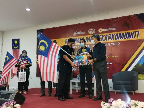 Zahidi (tengah) menyaksikan Mohamad (kanan) menyerahkan Jalur Gemilang kepada pasukan barisan hadapan pada program Merdeka@Komuniti Peringkat daerah Seremban di Dewan Eco Park Rantau di sini hari ini. 