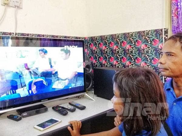 Simi Segar bersama cucunya menunjukkan televisyen yang baru dibeli sebagai satu cara meraikan kemudahan bekalan elektrik yang diterima penduduk.