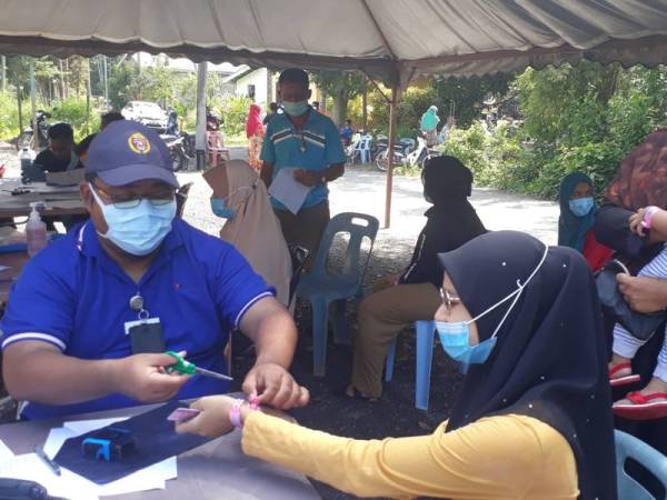 Pegawai kesihatan Daerah Padang Terap memotong gelang merah jambu di tangan penduduk yang terlibat dengan PKPD Secara Pentadbiran di Surau Kampung Ulu, Padang Sanai hari ini.