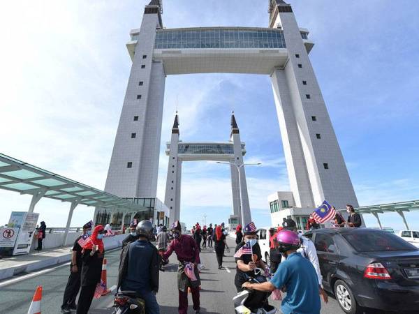 Kakitangan Primula Beach Hotel kelihatan mengedarkan Jalur Gemilang kepada para pengguna jalan raya yang melalui Jambatan Angkat Kuala Terengganu hari ini.