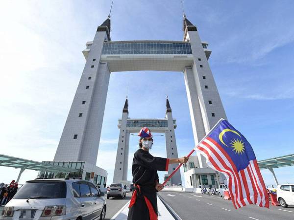 Kakitangan Primula Beach Hotel, Wan Tazilah Wan Harun mengibarkan Jalur Gemilang berlatar belakang Jambatan Angkat Kuala Terengganu hari ini.