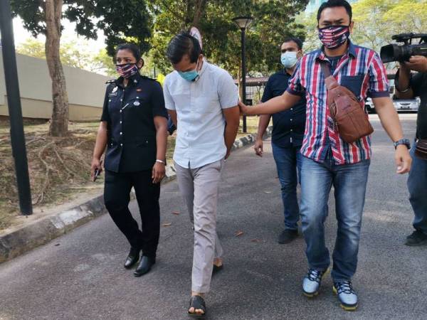 Tertuduh (depan, kiri) diiring polis di mahkamah.