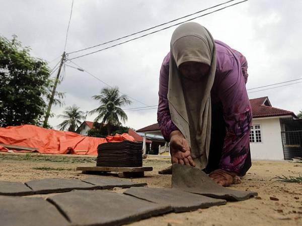 Noraini menyusun atap tersebut dan dijemur sebelum dimasukkan ke dalam tanur di Noraini Atap Bata Singhora, Kampung Pengkalan Baru.- Foto: Bernama