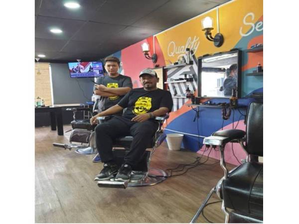 Tega (duduk) bersama seorang daripada staf di Mybudget Barbershop.