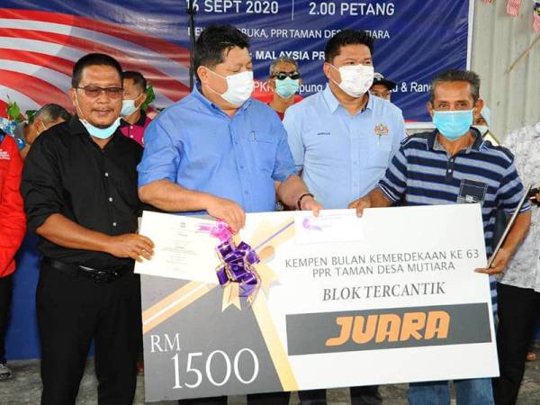 Mazlan (tengah) menyampaikan replika cek kepada pemenang Pertandingan Blok Tercantik Sempena Kempen Bulan Kẻmerdekaan ke-63 PPR Taman Desa Mutiara, Johor Bahru hari ini.