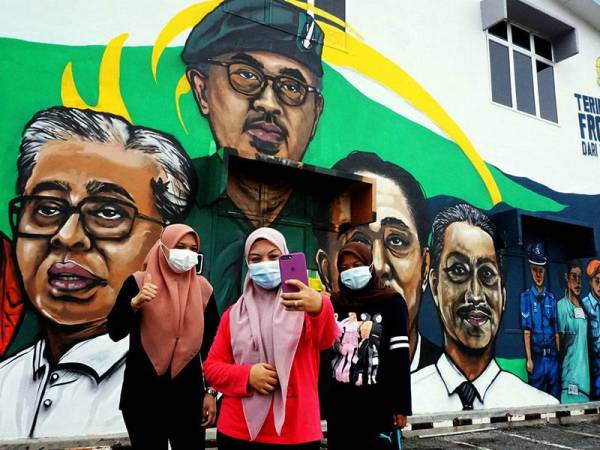 Penduduk Pendang, Anis Atikah Ismail, 22, (tengah) ditemani rakannya, Ayu Wahida Abdul Hadis, 27, (kanan) dan Farhana Mohd Nor, 24, (kiri) berswafoto di hadapan mural Majlis Daerah Pendang (MDP) bagi menghargai barisan frontliner yang bertungkus lumus memerangi pandemik COVID-19 di negara ini di pekan Pendang, hari ini.