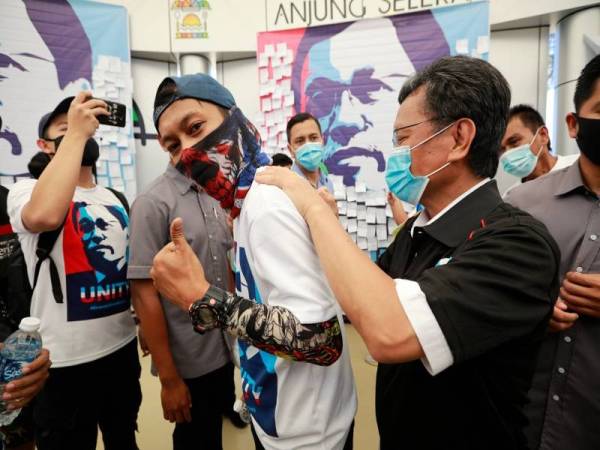 Mohd Shafie menurunkan tandatangan di belakang baju seorang belia pada Program Sabah Unity bersama belia di Teluk Likas, Kota Kinabalu hari ini.