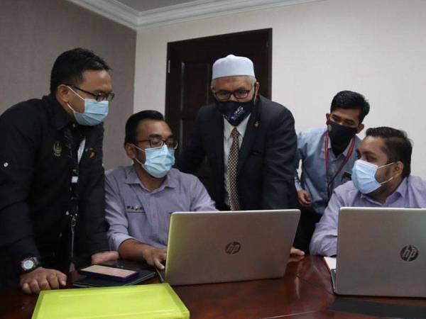 Razman (tengah) melihat data permohonan bantuan pelajar berasal dari Perak yang dikendalikan Pasak di pejabatnya di Ipoh hari ini.