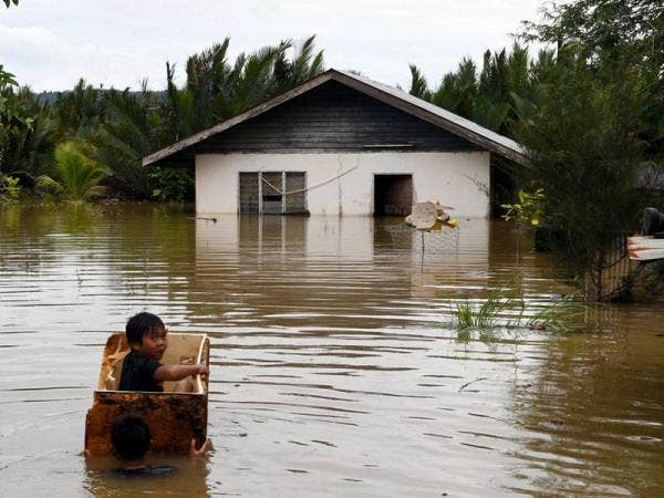 Dua kanak-kanak leka bermain air menggunakan kotak polistirena di depan sebuah rumah yang separuh tenggalam dengan air banjir di Kampung Paka Paka hari ini.