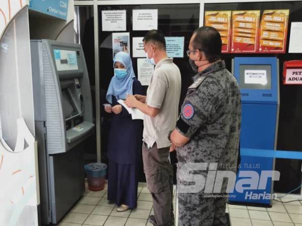 Salah seorang daripada tertuduh (tengah) melakukan urusan bayaran denda di mesin pembayaran di pekarangan Kompleks Mahkamah Kuala Terengganu hari ini dengan dibantu kakitangan mahkamah bertugas.
