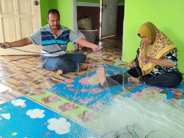Hasni (kiri) membantu Robeah menyiapkan tempahan pukat dari nelayan.