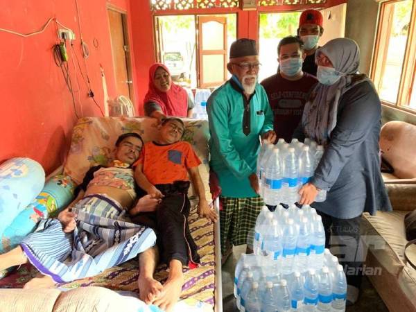 Nik Munirah Akmal (kanan) menyerahkan air minuman kepada Ismail di rumahnya di Kampung Tok Puchomg, Kedai Buloh hari ini. 