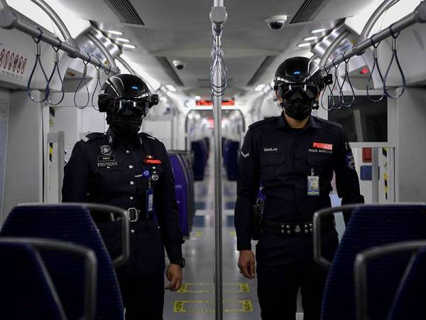 Anggota Polis Bantuan Kereta Api Tanah Melayu Berhad (KTMB) Siti Nabilla Isnariah Mohd Jonib (kiri) dan Muhd Amirul Shazlan Badrul Hisham (kanan) melakukan rondaan di dalam gerabak menggunakan topi keledar pintar bagi mengesan suhu badan pengguna yang menggunakan perkhidmatan awam Kereta Api Tanah Melayu (KTM) ketika tinjauan hari ini. - Foto Bernama