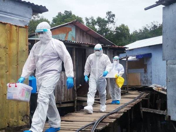 Petugas KKM lengkap berpakaian PPE sambil membawa kotak dipercayai mengandungi peralatan untuk ujian calitan penduduk di Kampung Lok Urai, Pulau Gaya, Kota Kinabalu.