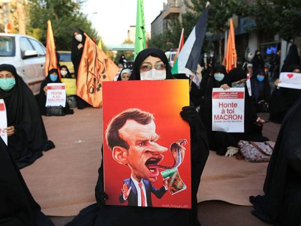 Seorang wanita membawa plakad tertera karikatur Macron berlidah bercabang seperti ular ketika protes di luar Kedutaan Perancis di Teheran, Iran.