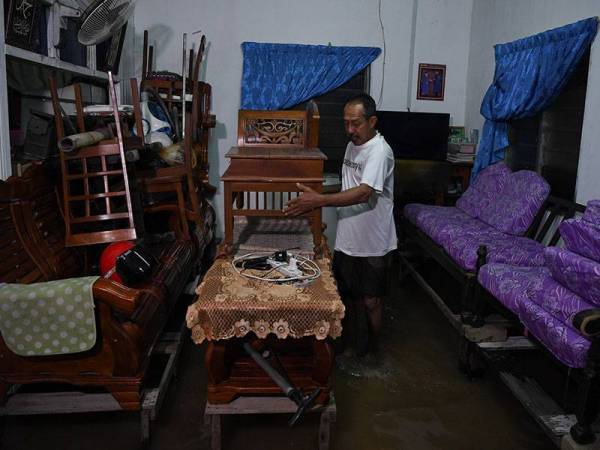 Abdullah Ibrahim, 63, mengangkat barangan yang ada dalam rumahnya untuk diletakkan di tempat lebih tinggi selepas rumahnya dilanda banjir kilat di Kampung Binjai Chendering malam ini.