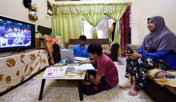 Suri rumah, Aulia Abidin, 43, bersama dua anaknya Ahmad Fareezuan Md Dusa,18 (kiri) dan Ahmad Farhan Md Dusa, 13, tekun mendengar siaran langsung Pembentangan Belanjawan 2021 oleh Tengku Zafrul hari ini. - Foto Bernama
