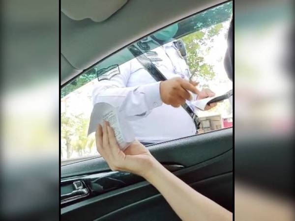 Tangkap layar video yang tular ketika anggota trafik mengeluarkan saman ke atas pemandu yang menggunakan telefon bimbit dengan tangan kiri semasa memandu di Jalan Dato Md Zain, Melaka Tengah semalam.