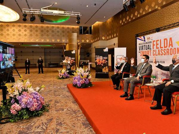 Mohd Radzi (tengah) Mustapa dan Idris melambai tangan kepada pengetua, guru dan pelajar SMK Lurah Bilut ketika berinteraksi secara langsung dari Menara Felda di Kuala Lumpur hari ini.