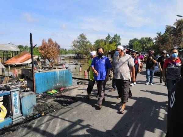 Ahmad ( kiri) meninjau keadaan rumah penduduk Kampung Sri Dungun yang hangus terbakar dalam kejadian Isnin lalu.
