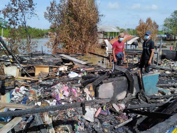 Rosmaini ( kiri) menunjukkan keadaan rumahnya di Kampung Sri Dungun di sini yang hangus terbakar dalam kejadian Isnin lalu.
