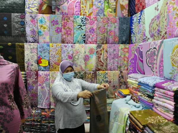 Kamariah mengemas batik jualannya, sambil menunggu pelanggan datang