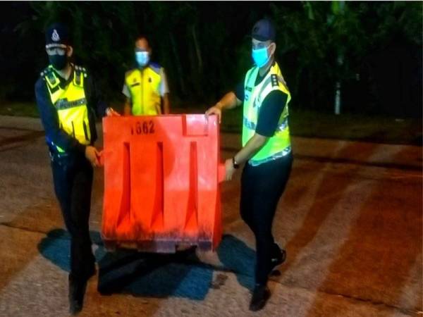 Ahmad Shukri (kiri) mengangkat penghadang jalan di sekatan jalan raya PKPB di hadapan Balai Polis Alor Janggus, tengah malam tadi.