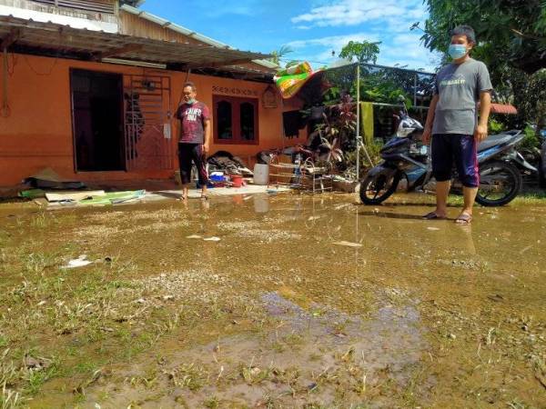 Shahri (kanan) dan Mohd Khir menunjukkan paras air yang naik sehingga paras dada semalam telah mulai surut, hari ini.