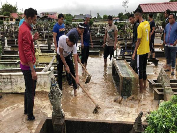 Penduduk mencangkul tanah membuat lorong bagi mengalirkan air keluar dari kawasan Tanah Perkuburan Islam Kubur Dato, Tumpat hari ini.