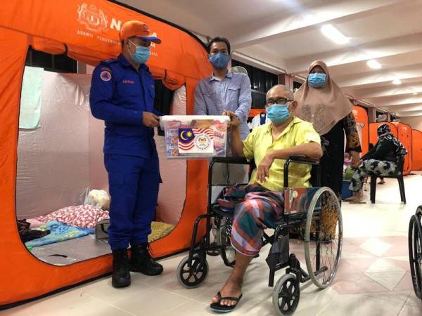 Nik Hassan (kanan) bersama isteri, Che Saluma Saleh, 44, menerima Kid Makanan Permulaan Banjir daripada Agensi Pengurusan Bencana Negara (NADMA) yang disampaikan Pegawai Angkatan Pertahanan Awam Kota Bharu, Leftenan Mohd Safiyan Ibrahim (kiri) dan Pengerusi Banjir Daerah Pendek, Mohd Syaqi Ahmad.