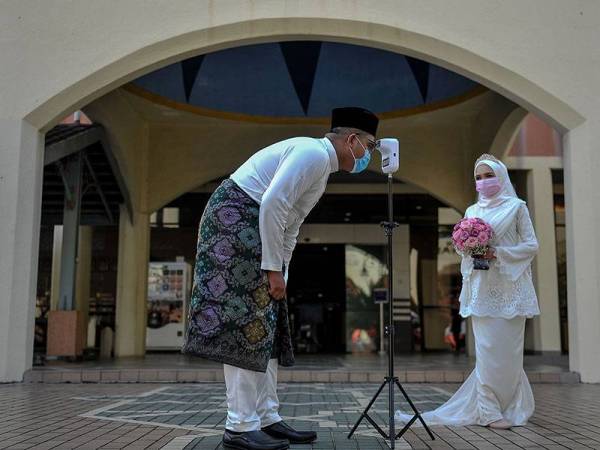 Kelihatan pasangan pengantin Mohammad Shaiful Nizam Rohadi (kiri) dan Nur Ayuni Abd Rahman (kanan) mematuhi prosedur operasi standard (SOP) dengan memakai pellitup muka dan mengimbas suhu badan pada majlis resepsi perkahwinan ketika tinjauan di Jabatan Agama Islam Wilayah Persekutuan (JAWI) hari ini. 