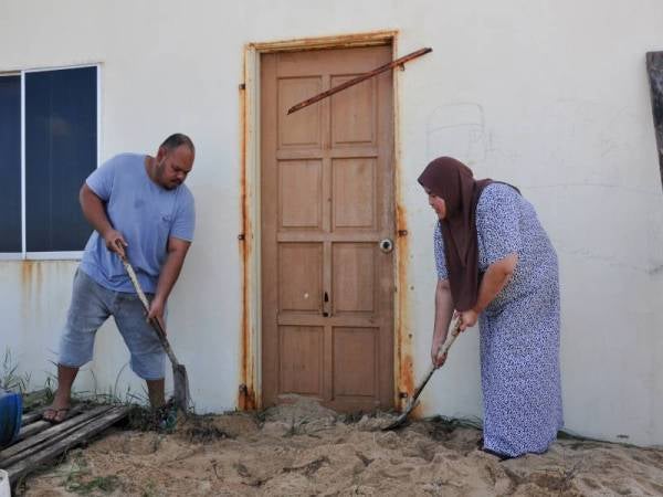 Mangsa air pasang besar, Abd Razak Mohd Zaid, 30, (kiri) dan isterinya Nurul Hafizah Zulkifli, 32, (kanan) mengorek pasir yang terkumpul di hadapan pintu rumah mereka ketika tinjauan di Kampung Pengkalan Atap, Kuala Besut. - Foto Bernama