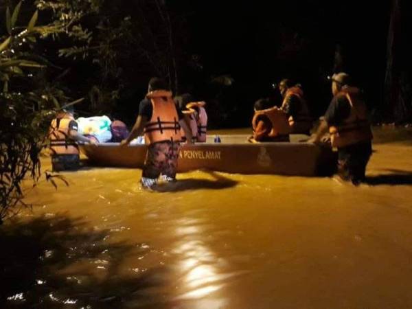 Anggota bomba membantu memindahkan mangsa banjir di Kampung Chenua, Raub ke PPS di balai raya kampung itu malam tadi. Foto JBPM Pahang.