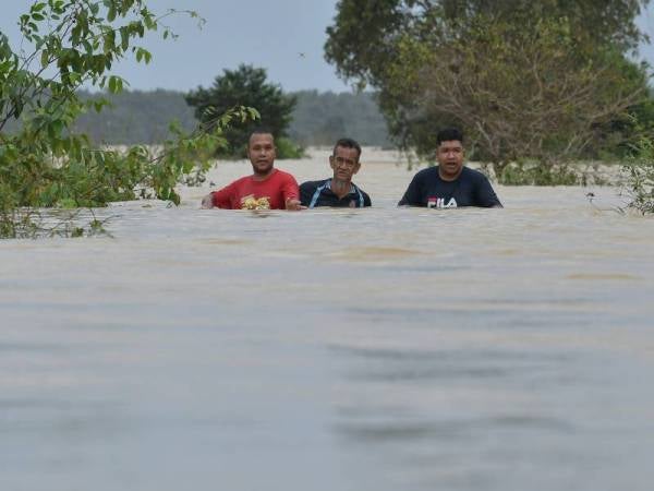 Zulkifli Ishak, 53, (tengah) bersama rakan-rakan Mohd Zaki Sata, 31, (kiri) dan Wan Mohd Shahiran Wan Zalani, 27, (kanan) meredah air untuk pergi ke pukat ikan yang dipasang di kawasan paya ketika tinjauan di Kampung Permaisuri. - Foto Bernama